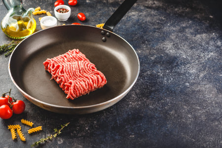 Fresh raw minced beef in frying pan and ingredients over dark background. Top view or flat-lay.