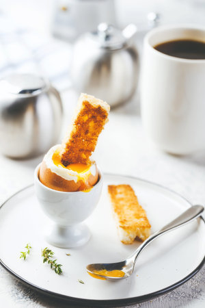 Soft boiled egg for breakfast with toasts and coffee cup in background