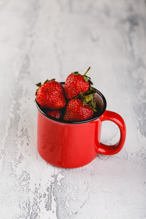 Fresh Strawberries in red enamel cup on grey backgroundの写真素材