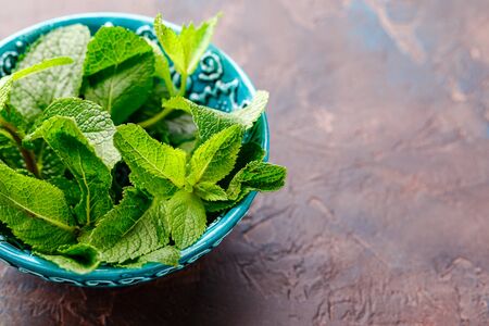 Fresh mint leaves in the ceramic bowl on the broun concrete background. Healthy vegetarian food concept. Close up. Place for textの写真素材