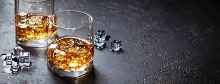 Two glasses of whiskey with ice on dark background with reflection. Alcohok drink. Space for text. Long wide bannerの写真素材