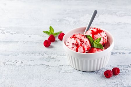 Raspberry ice cream balls with syrup, berries and mint leaves in white bowlの写真素材