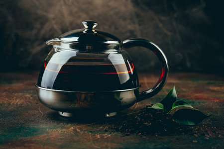 Glass transparent teapot and two glass cups with black tea on a dark table