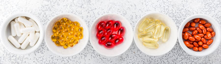 Assorted pharmaceutical medicine pills, tablets and capsules on white bowls. Top view