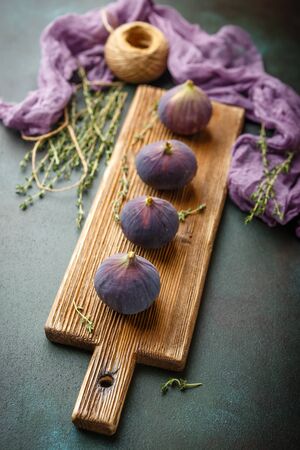 Juicy fresh fig fruits on wooden cutting board on dark green backgroundの写真素材
