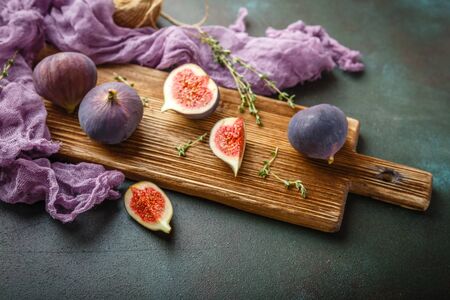 Juicy fresh whole fig fruits and one cut figs on wooden cutting board on dark green backgroundの写真素材