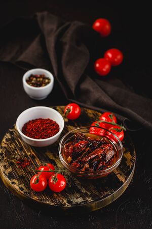Fresh cherry tomatoes, sun-dried tomatoes and dried tomatoes with rosemary sprigs on a wooden cutting board on a dark background.の写真素材