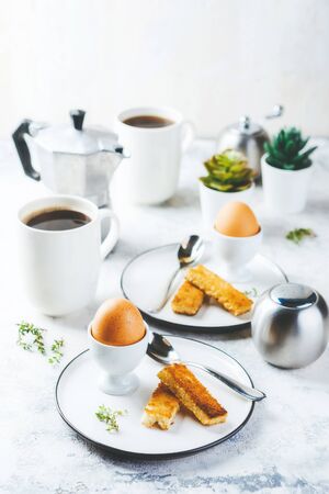 Soft boiled egg for breakfast with toasts and coffee cup in backgroundの写真素材