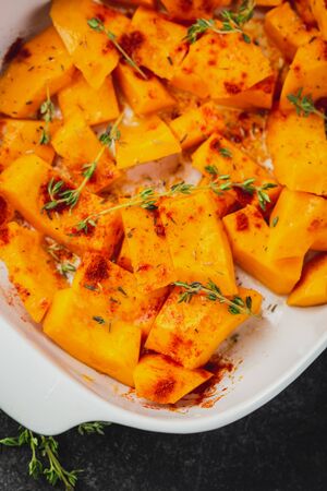Raw pumpkin sliced in small pieces with thyme in a baking dish on a wooden background.の写真素材