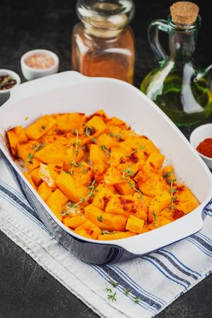 Raw pumpkin sliced in small pieces with thyme in a baking dish on a wooden background.の写真素材