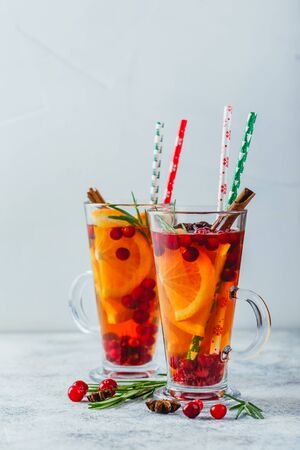 Hot tea with orange slices, cranberries and rosemary in tall glasses. Hot drinks for winter and Christmas. Place for textの写真素材