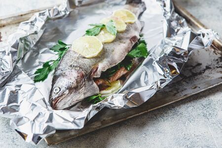 Fresh Rainbow raw trout with parsley and lemon in foil on light pan on grey background. Healthy food. Cooking concept.の写真素材