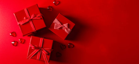 Two red boxes with gifts and bows on a red background with small glass hearts. Symbol of love and...