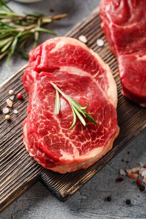 Three pieces of traditional thin steak cut from the tenderloin on wooden cutting board with olive oil, salt, rosemary and pepper. Raw Black Angus Prime meat steaks for grilling or frying pan. Close upの写真素材