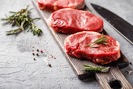 Three pieces of traditional thin steak cut from the tenderloin on wooden cutting board with olive oil, salt, rosemary and pepper. Raw Black Angus Prime meat steaks suitable for grilling or frying pan.の写真素材