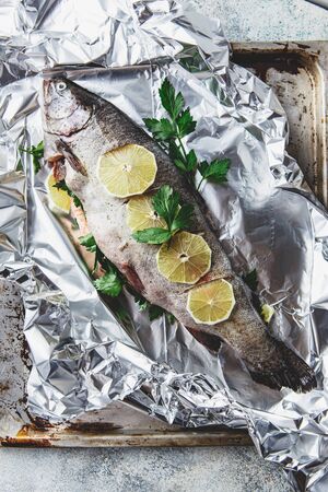 Fresh Rainbow raw trout with parsley and lemon in foil on light pan on grey background. Healthy food. Cooking concept. Top viewの写真素材