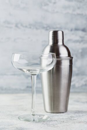 Empty wide champagne glass and metal shaker on a light background. Set of dishes for making cocktailsの写真素材