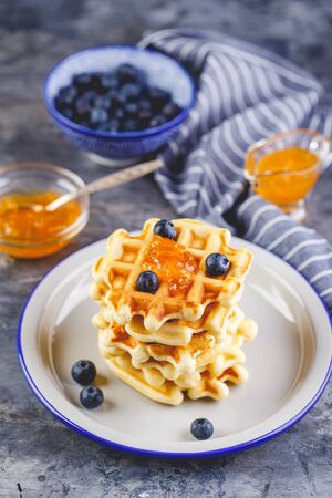 Traditional belgian homemade waffles with blueberry, honey and orange jam on plate on gray background.の写真素材