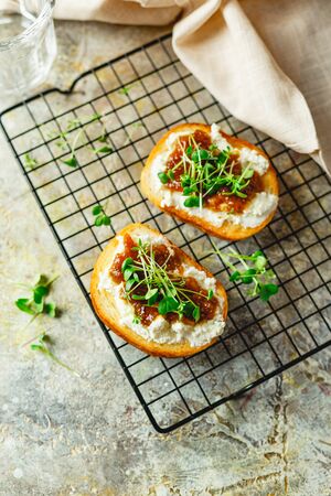 Canape or crostini with toasted baguette, cottage cheese, fig jam and microgreen on metal grid. Delicious snack, ideal as an aperitifの写真素材