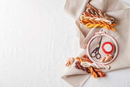 Set for embroidery. Linen fabric, patterns for embroidery, hoop, thread of yellow and brown colors and needles. Copy space, top viewの写真素材