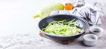 Zucchini noodles in frying pan on white background. Vegetarian dish. Copy space. Long wide bannerの写真素材