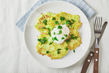 Vegetable zucchini pancakes with poached egg on white plate. Top view