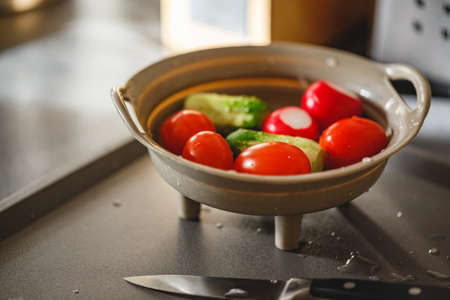 Washed vegetables in a colander on the kitchen table for making salad - radishes, cucumbers, tomatoes, herbsの写真素材