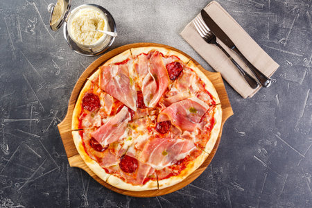 Pizza with salami and prosciutto on wooden board on dark backgroundの写真素材