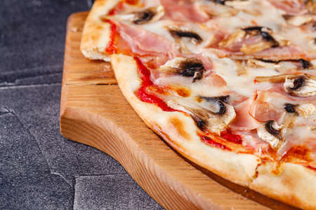 Pizza with ham and mushrooms on a wooden board on a dark background. Close-upの写真素材