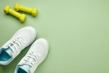Creative flat lay of sport and fitness equipment. Women's white sneakers and green dumbbells on a light green background.の写真素材