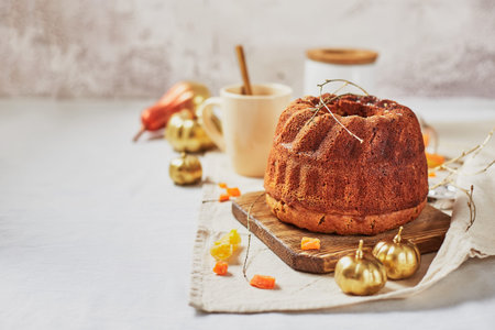 Homemade autumn carrot or pumpkin bundt cake with candied fruits, cup of tea and golden decorative...