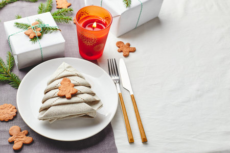 Christmas festive table setting, napkin in the form of Christmas tree on a plate on white tablecloth...