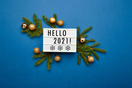 White light box with text Hello 2021, fir branches and golden christmas balls on blue background. Flat lay, top view, copy space. Christmas frame, New year banner mockupの写真素材