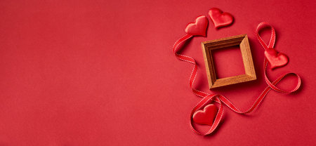Wooden frame and Valentines day hearts and decorations on red background. Top view with copy space. Valentines day concept.の写真素材