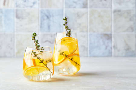 Refreshing cocktail with ice, orange and thyme. Refreshing summer homemade alcoholic or non-alcoholic cocktail or mocktail, or Detox infused flavored waterの写真素材