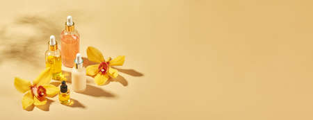 Cosmetic care products in glass bottles with orchid flowers - serums, cream, gel, oils. Concept for face and body care, wellness and spa, tropical relaxation.の写真素材