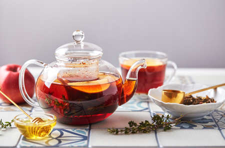 Fruit tea with apples and thyme in glass teapot and cup on table made of colored tilesの写真素材