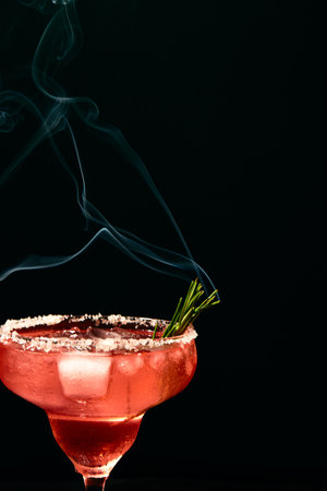 Alcoholic or non-alcoholic margarita type cocktail with ice and steaming rosemary branch on dark backgroundの写真素材