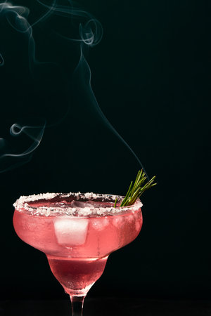 Alcoholic or non-alcoholic margarita type cocktail with ice and steaming rosemary branch on dark backgroundの写真素材