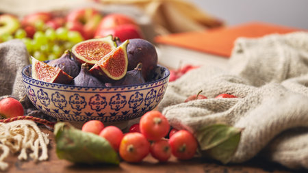 Dish with figs, apples and grapes with warm cozy knitwear, autumn leaves and apples.