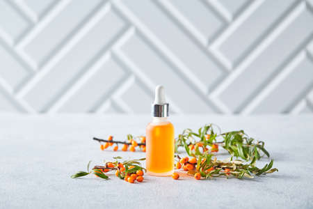 Glass bottle with sea buckthorn oil, berries and branches of sea buckthorn on light backgroundの写真素材