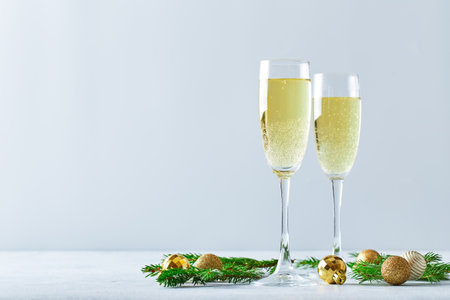 Glasses with sparkling wine type champagne with fir branches and golden Christmas tree decorations on light backgroundの写真素材