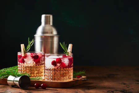 Alcoholic cocktail or non-alcoholic cocktail with vodka and cranberries with ice, shaker, jigger and bar spoon, fir branches and glowing garland for christmas on wooden backgroundの写真素材