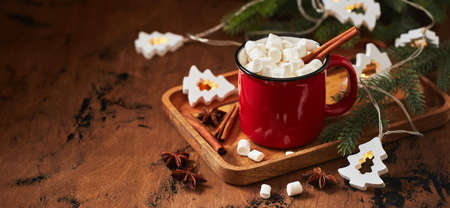 Red cup of hot cocoa with marshmallows on wooden table with christmas tree for christmasの写真素材