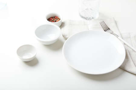 Empty white plate with a fork and small bowls on a light backgroundの写真素材