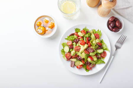 Salad with lettuce, cucumbers, tomatoes, olives and avocados in white plate on the table.の写真素材