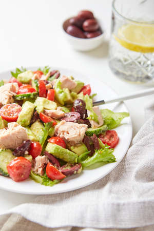 Salad with tuna, lettuce, cucumbers, tomatoes, olives and avocados in white plate on the table.の写真素材