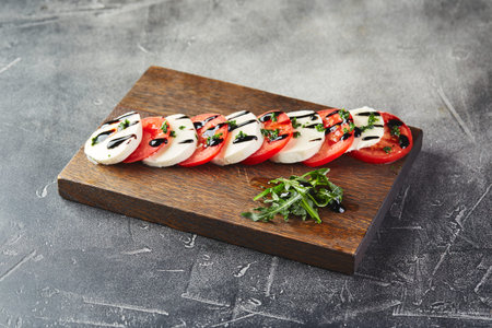 Caprese salad with mozarella cheese, tomatoes and basil on wooden cutting board