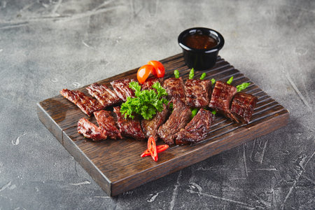 Sliced steak with sauce in sauceboat on wooden cutting board
