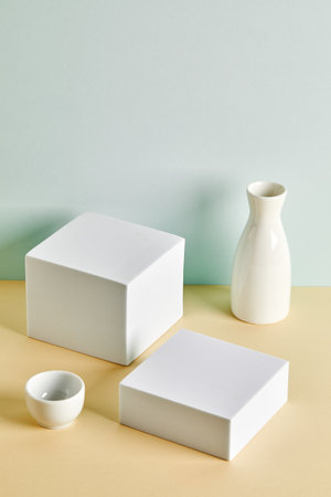 Two rectangular white podiums with white vase and small bowl on light backgroundの写真素材